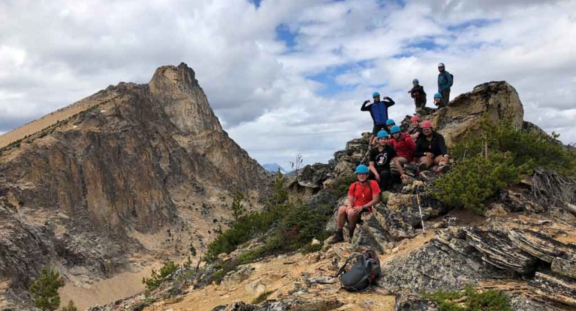 a group of students smile for a photo at the summit of a mountain